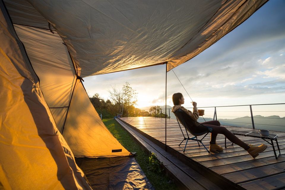 A traveler relaxing on a wooden deck beside a tent at sunset