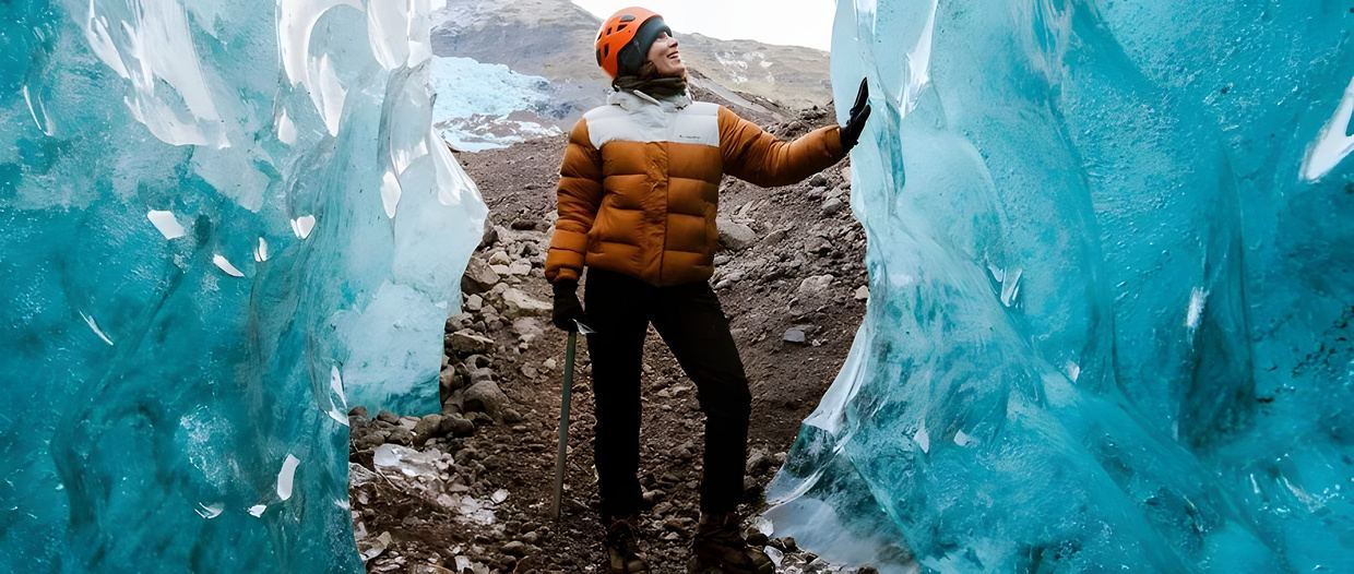 A climber in an orange jacket inside a blue glacier ice cave