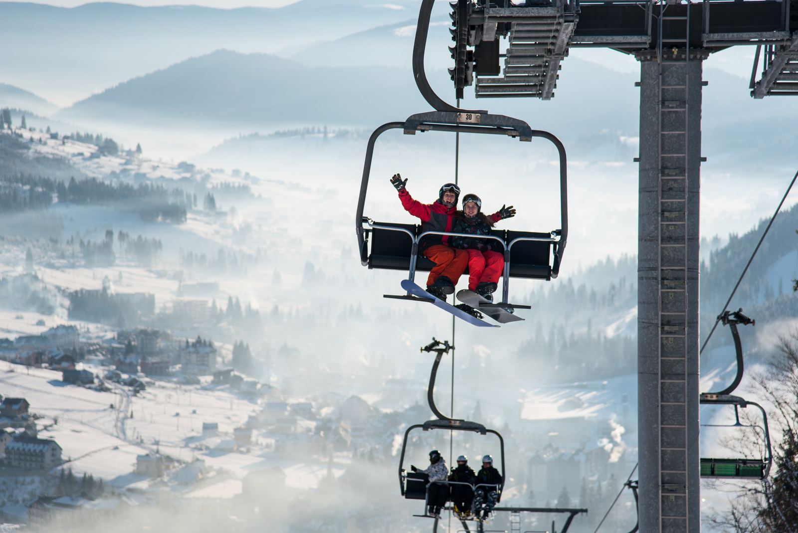 Two skiers waving from a chairlift above a misty snowy valley